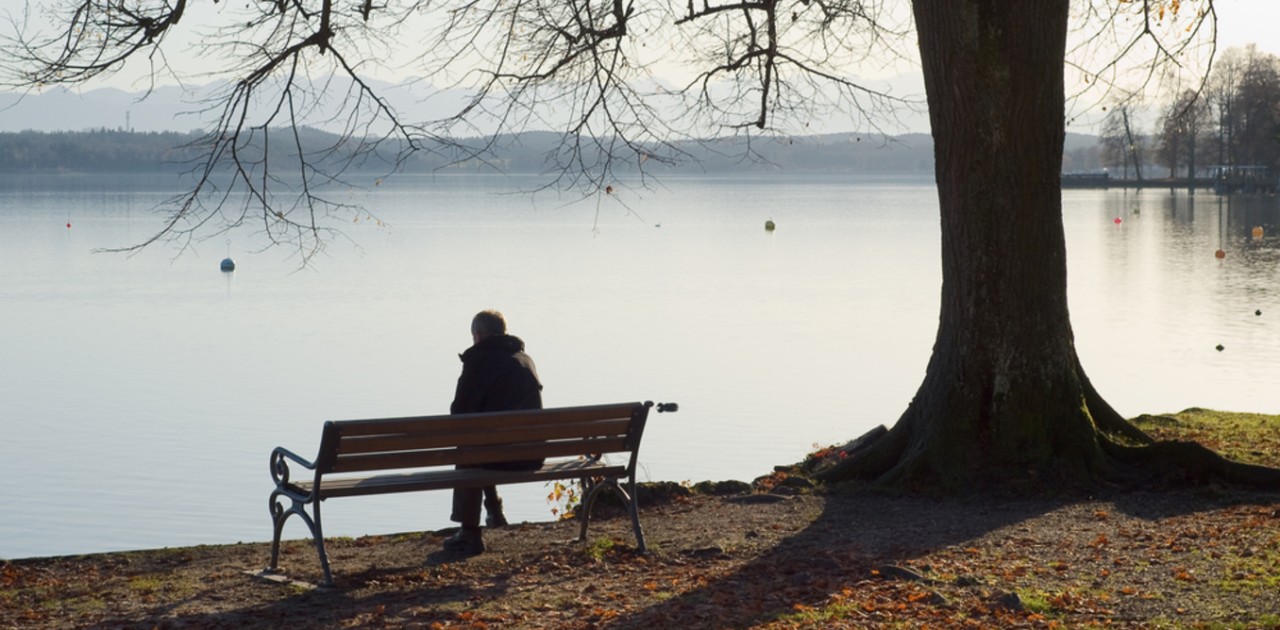 Man sitting alone on a bench by a lake